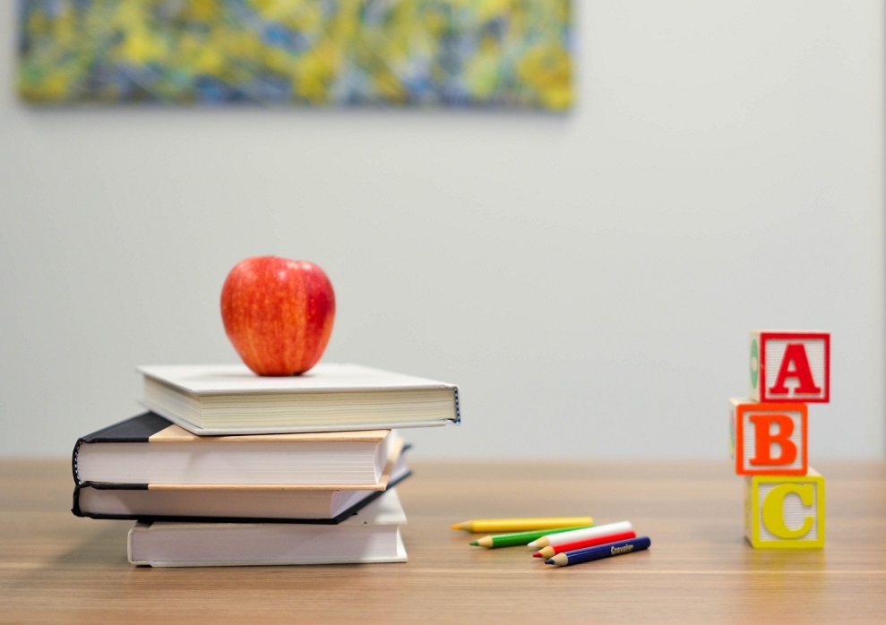 A school desk with books, an apple and stationery.