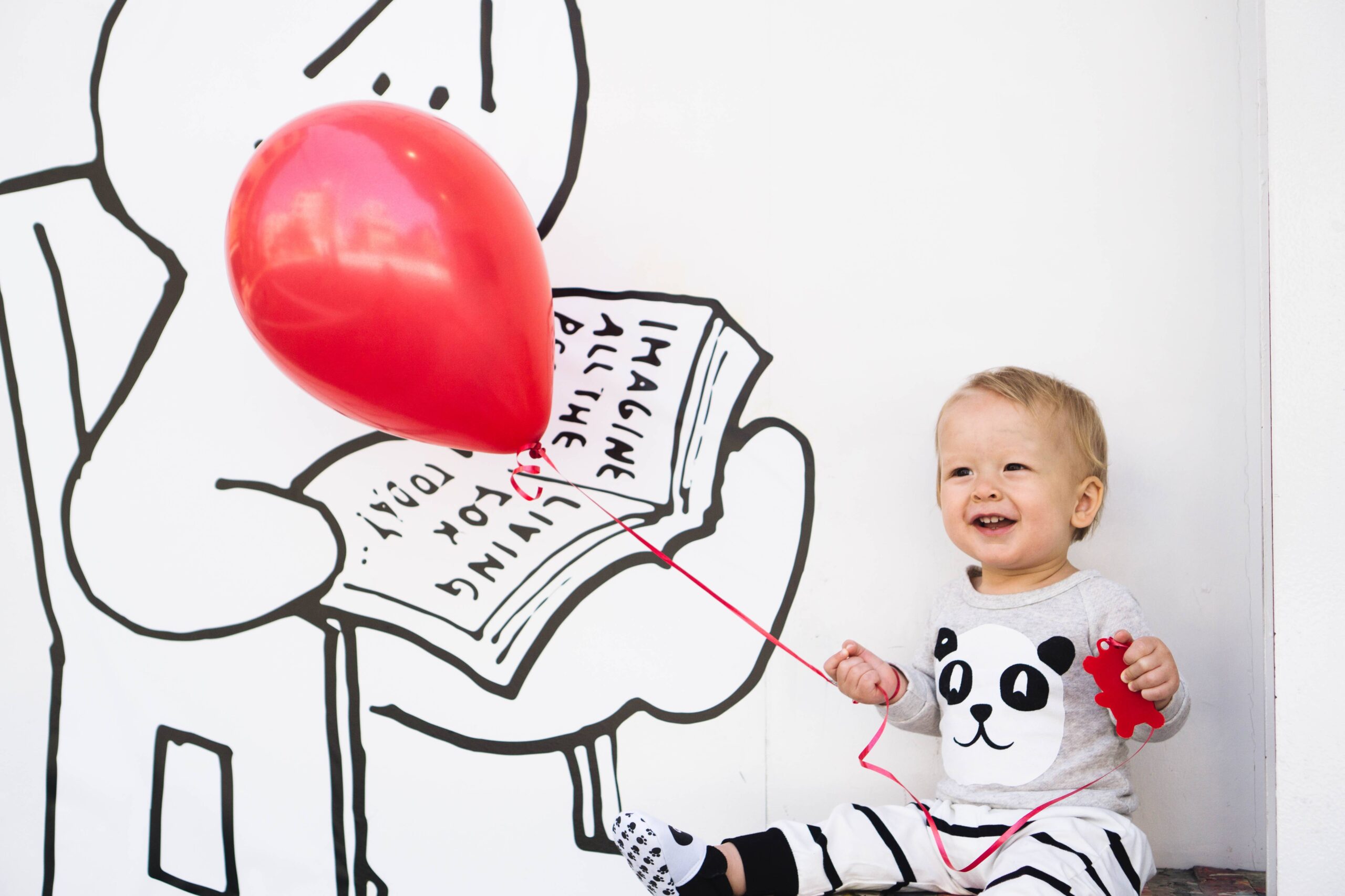 a baby holding a red balloon smiling