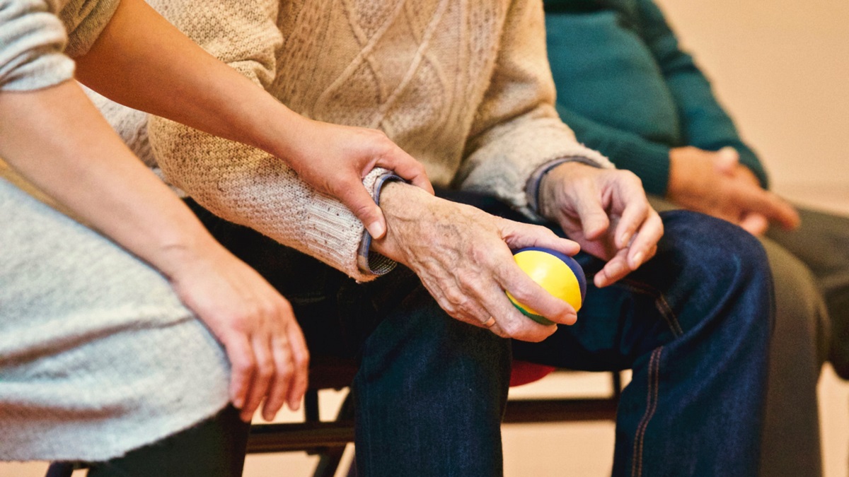 A carer holds hands with an elderly person
