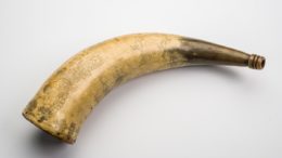 Cow’s horn adapted to be a ‘powder flask’ for gunpowder. These were carried on a strap and used to prime muskets and early firearms. It is engraved with many images including the Royal coat of arms and a mermaid.