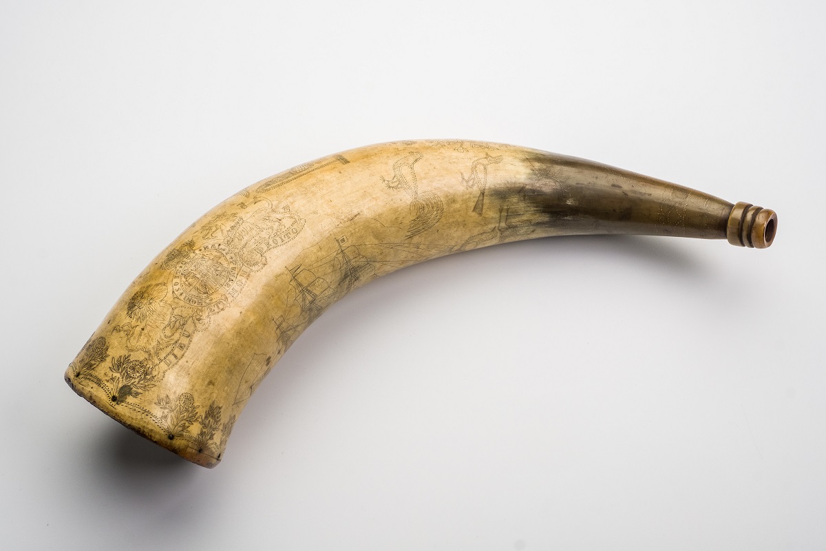 Cow’s horn adapted to be a ‘powder flask’ for gunpowder. These were carried on a strap and used to prime muskets and early firearms. It is engraved with many images including the Royal coat of arms and a mermaid.