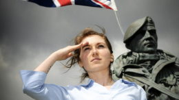 a young woman salutes next to a statue and the union jack flag