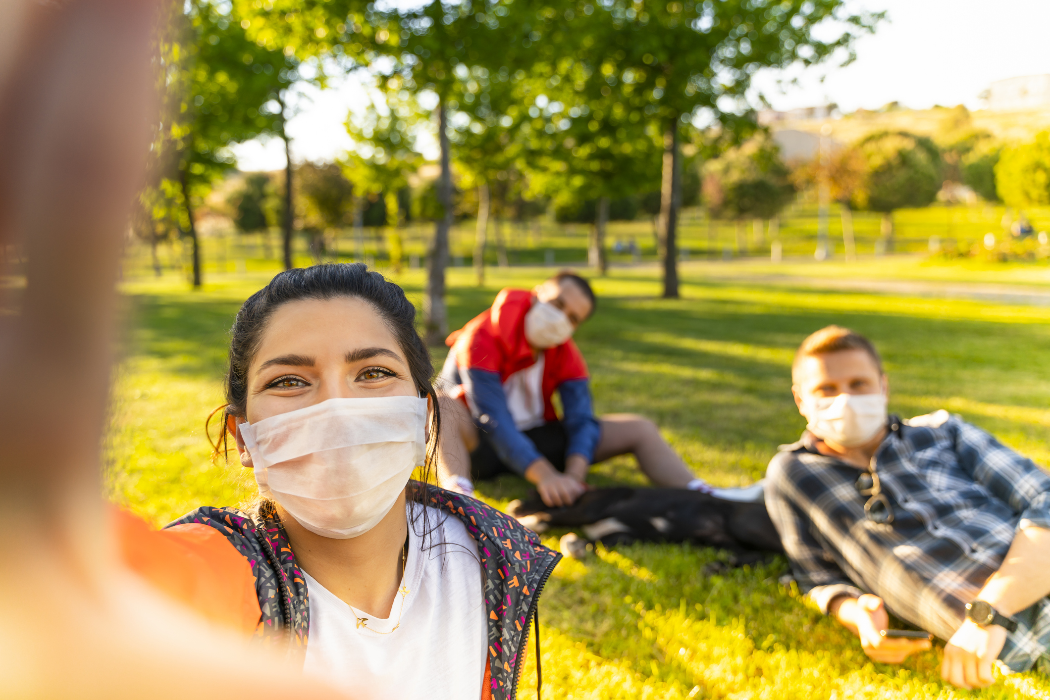 Cheerful university student taking selfie with friends sitting on grass