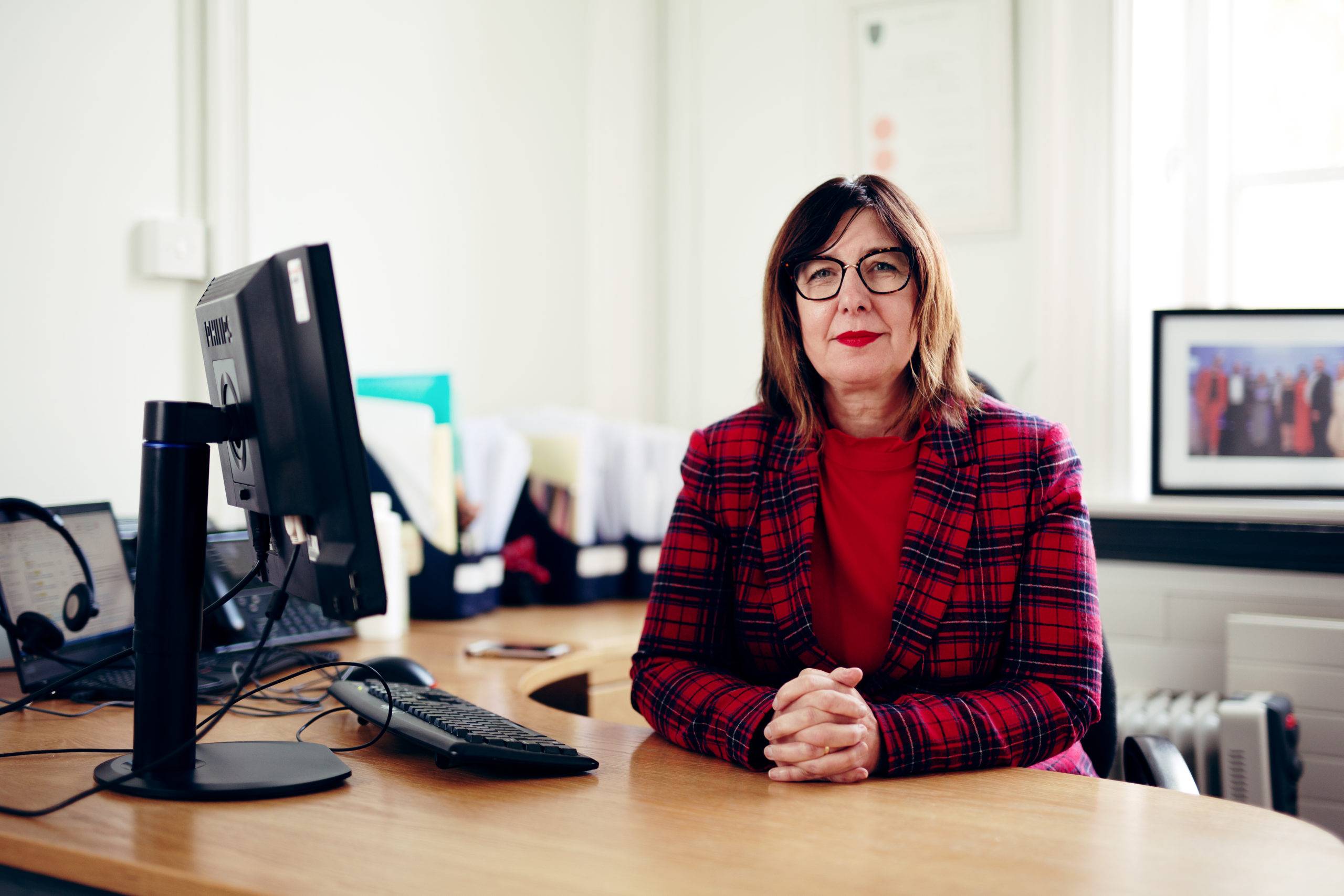 Julia Weldon, Hull's Director of Public Health sits at her desk. She is wearing a red check jacket and has a serious expression