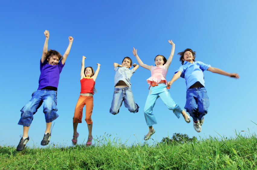 five children jump joyfully outside, in sunny weather. The picture is taken from ground-level, looking up at them
