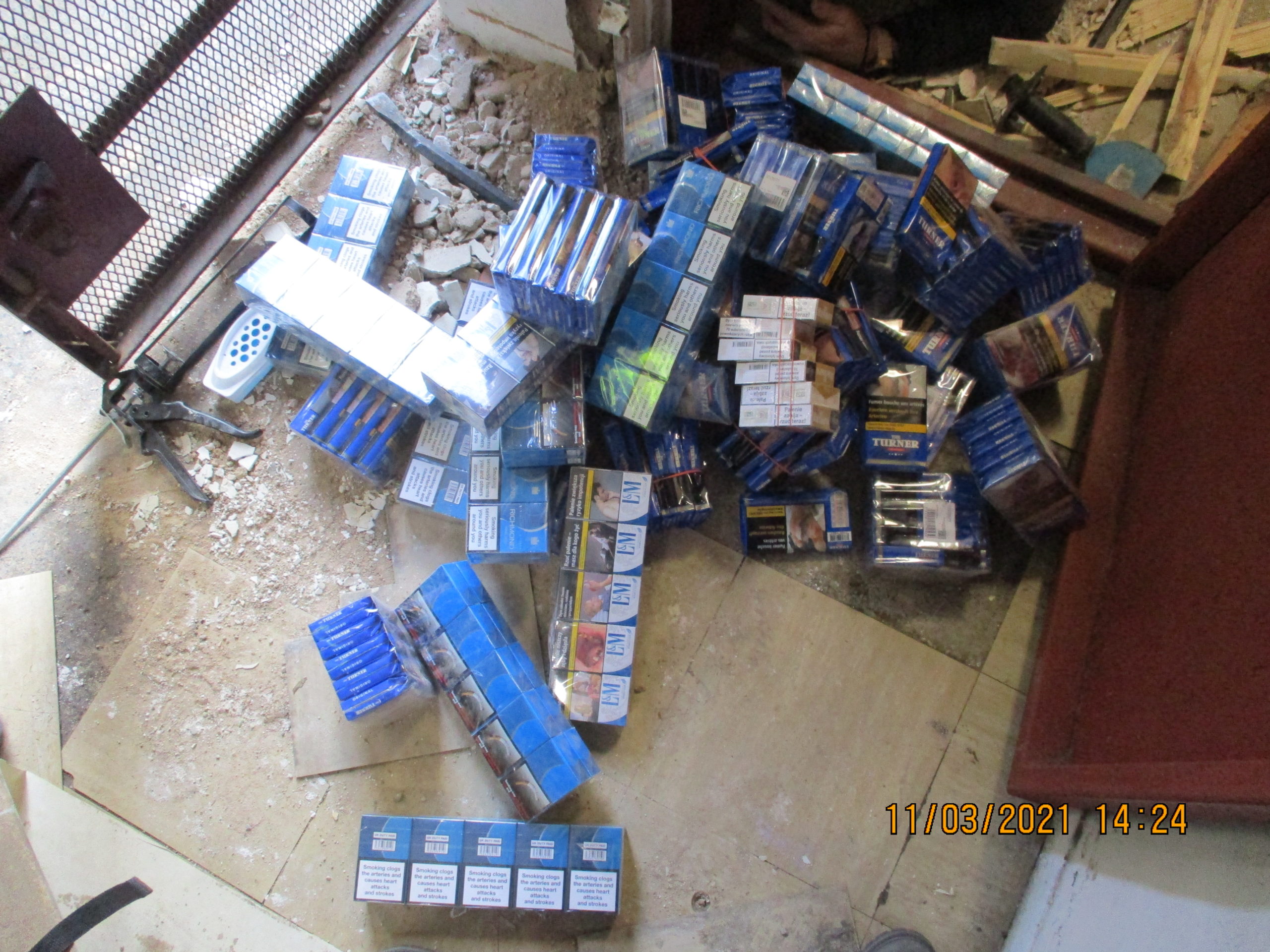 Packets of counterfeit cigarettes and tobacco sit on a concrete floor after being recovered from beneath a concrete floor
