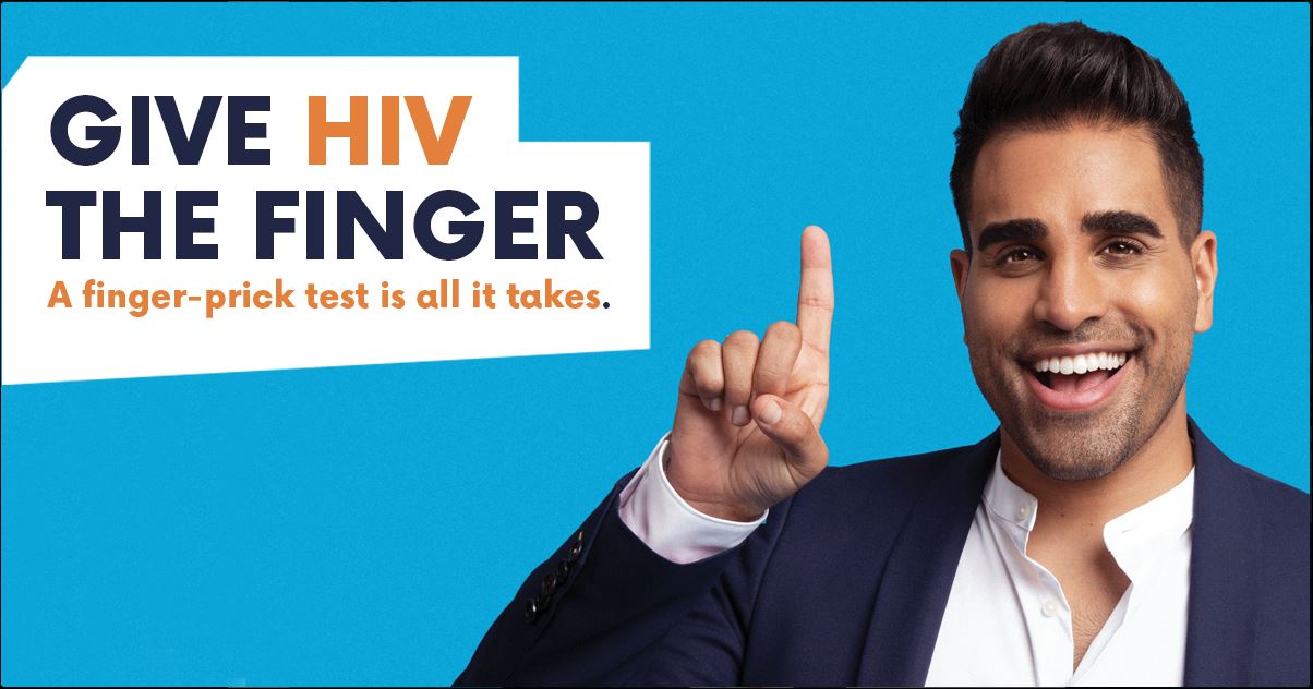 Celebrity Doctor Ranj Sing poses in front of a plain blue background. He is smiling and pointing to bright orange and blue text, which says: Give HIV the finger. A finger-prick test is all it takes