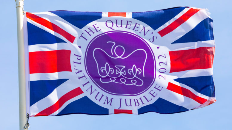 A flag commemorating the Queen's Platinum Jubilee, flying over a clear blue sky.