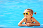 Smiling young girl in sunglasses in a swimming pool on a sunny day.