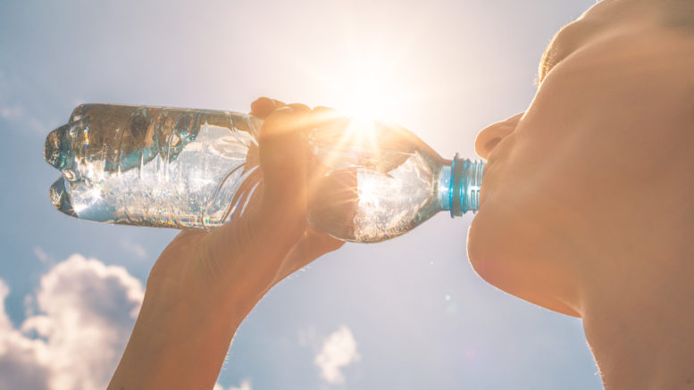 Young woman drinking bottle of water with the sun shining above