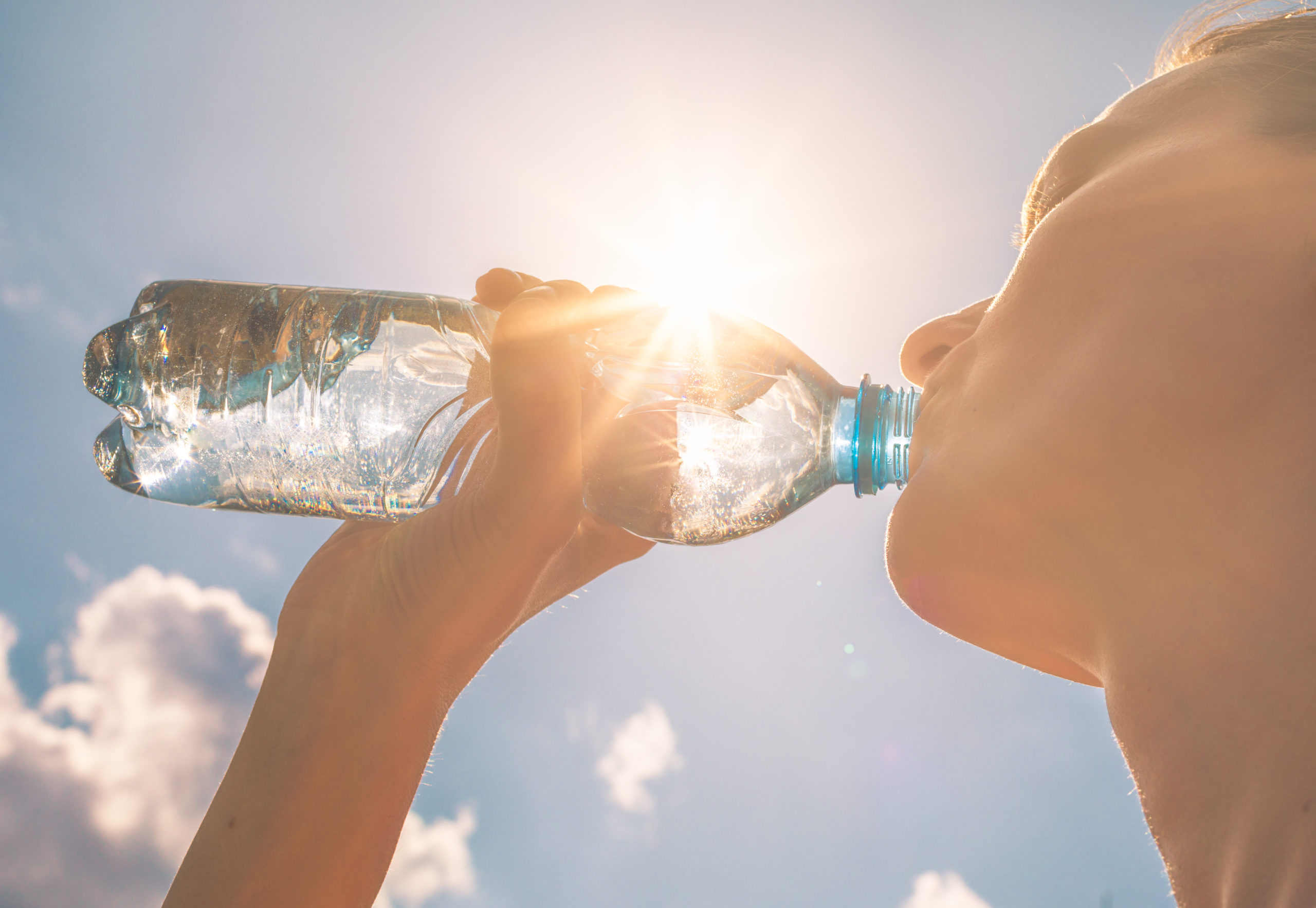 Young woman drinking bottle of water with the sun shining above