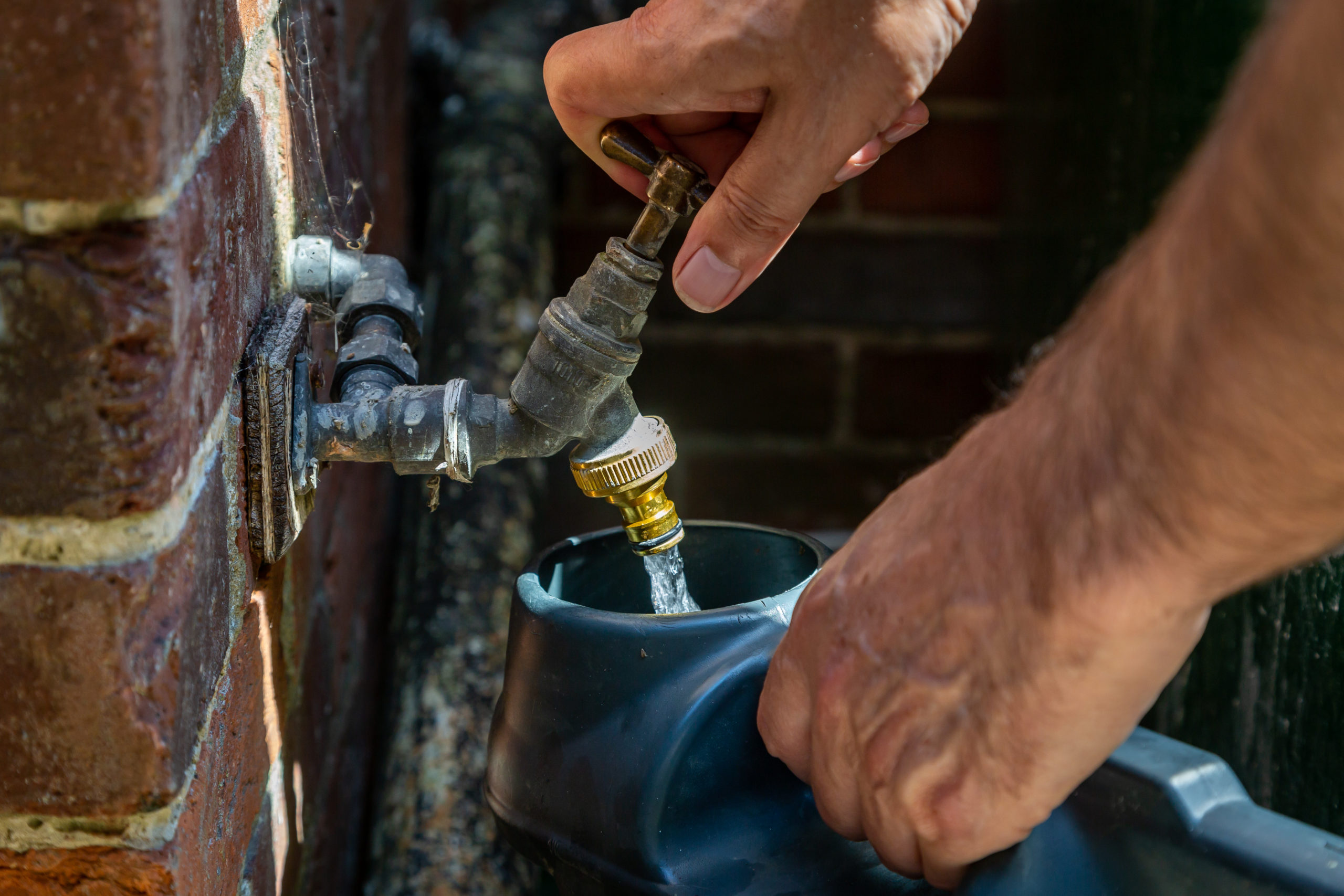 A man filling a watering can from an outside tap during a hosepipe ban in the UK