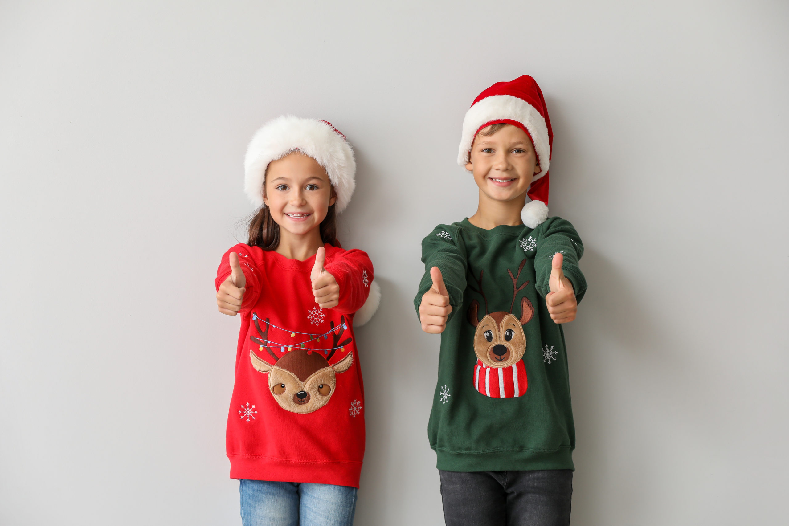 Funny children in Christmas sweaters showing thumb-up on light background