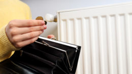 a person takes coins out of a purse. In the background, a radiator is visible. We can only see the person's hand and sleeve.