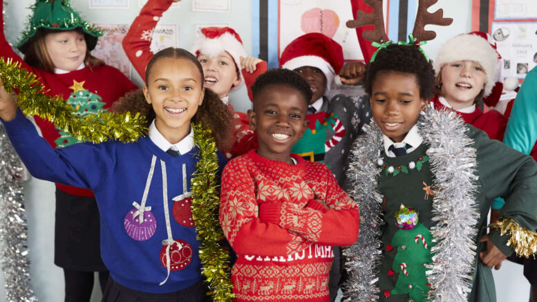 A group of children wearing Christmas jumpers and tinsel