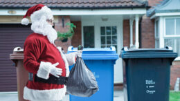 Santa claus walking towards some bins carrying a filled bin liner