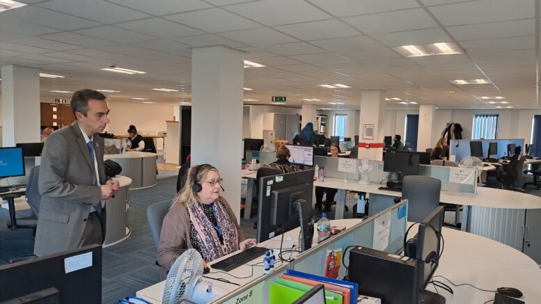 An open plan office, which serves as thew Hull City Council call centre. council leader Mike Ross stands behind a call handler, who is working at a screen with a headset on