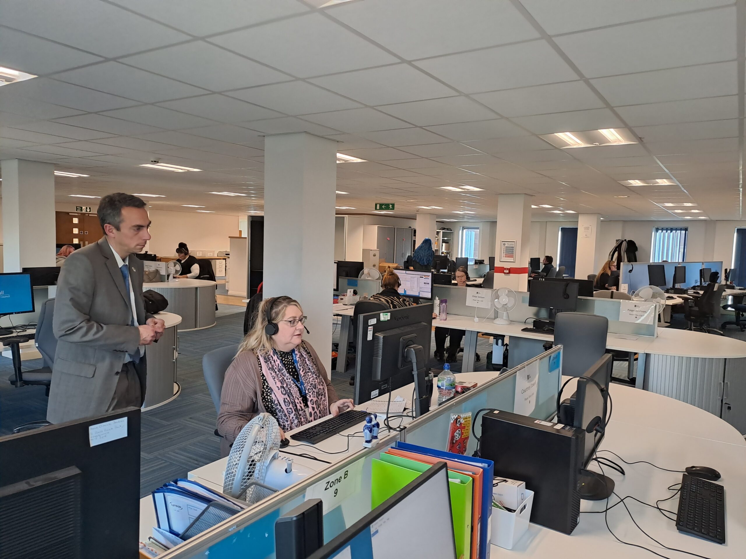 An open plan office, which serves as thew Hull City Council call centre. council leader Mike Ross stands behind a call handler, who is working at a screen with a headset on