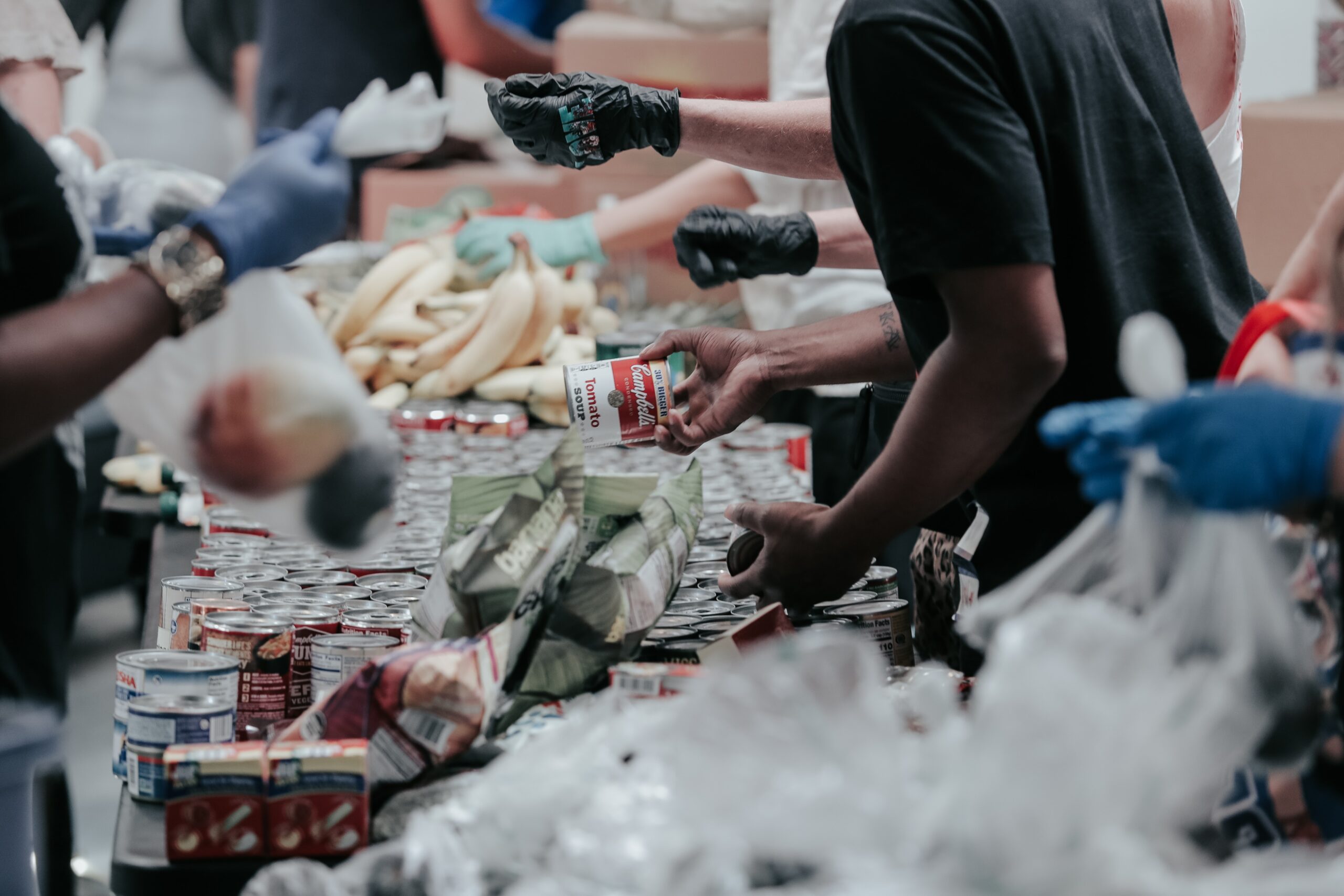 a shot of goods being distributed at a food bank. People's arms and bodies are in the photo, but their faces are not