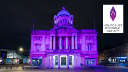 Hull City Hall illuminated in purple light at night. The logo for Holocaust Memorial Day with the text "Holocaust Memorial Day 27/01" appears in the corner on the picture