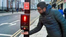 A man holding his hand under a push button unit at a pedestrian crossing fitted with Smart Cross technology