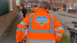 A Hull City Council worker cutting grass verges. He is seen from behind wearing a high-visibility jacket emblazoned with the "Love Your Neighbourhood" logo