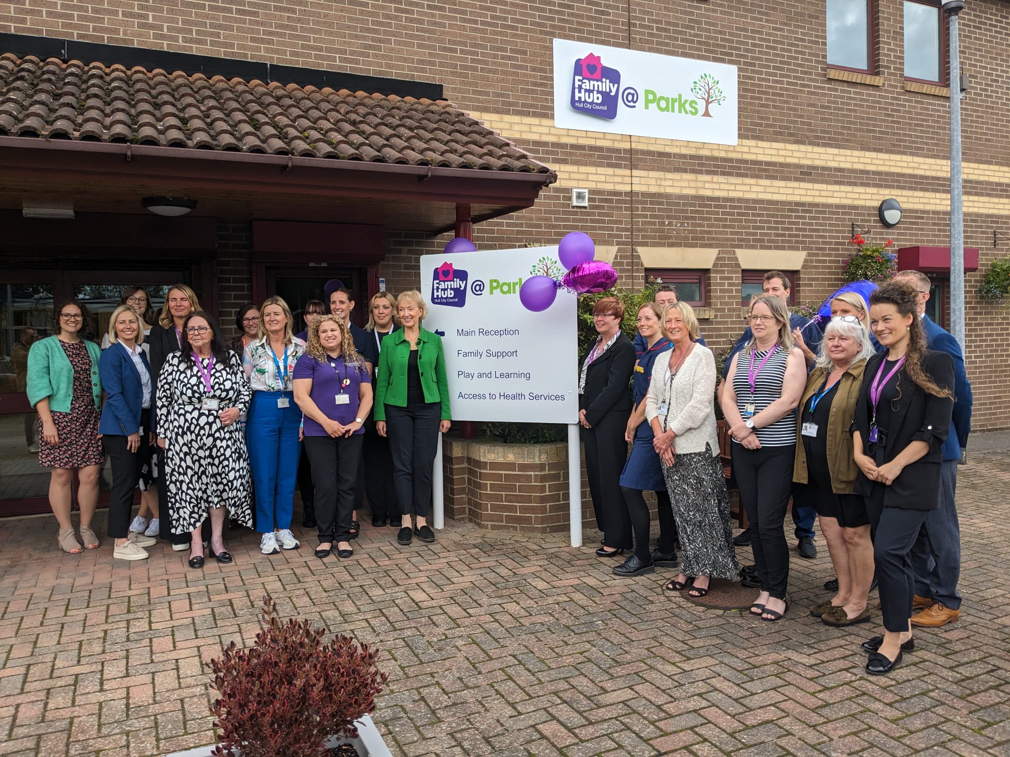 A group of people celebrating the Parks Family Hub launch, gathered around the newly unveiled sign.