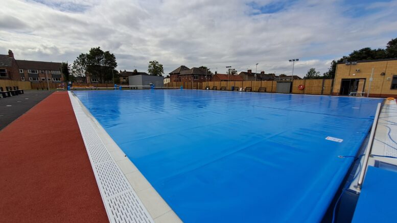 A view of the new outdoor lido pool at Albert Avenue with blue pool covers over the water and red walkway surrounding it.