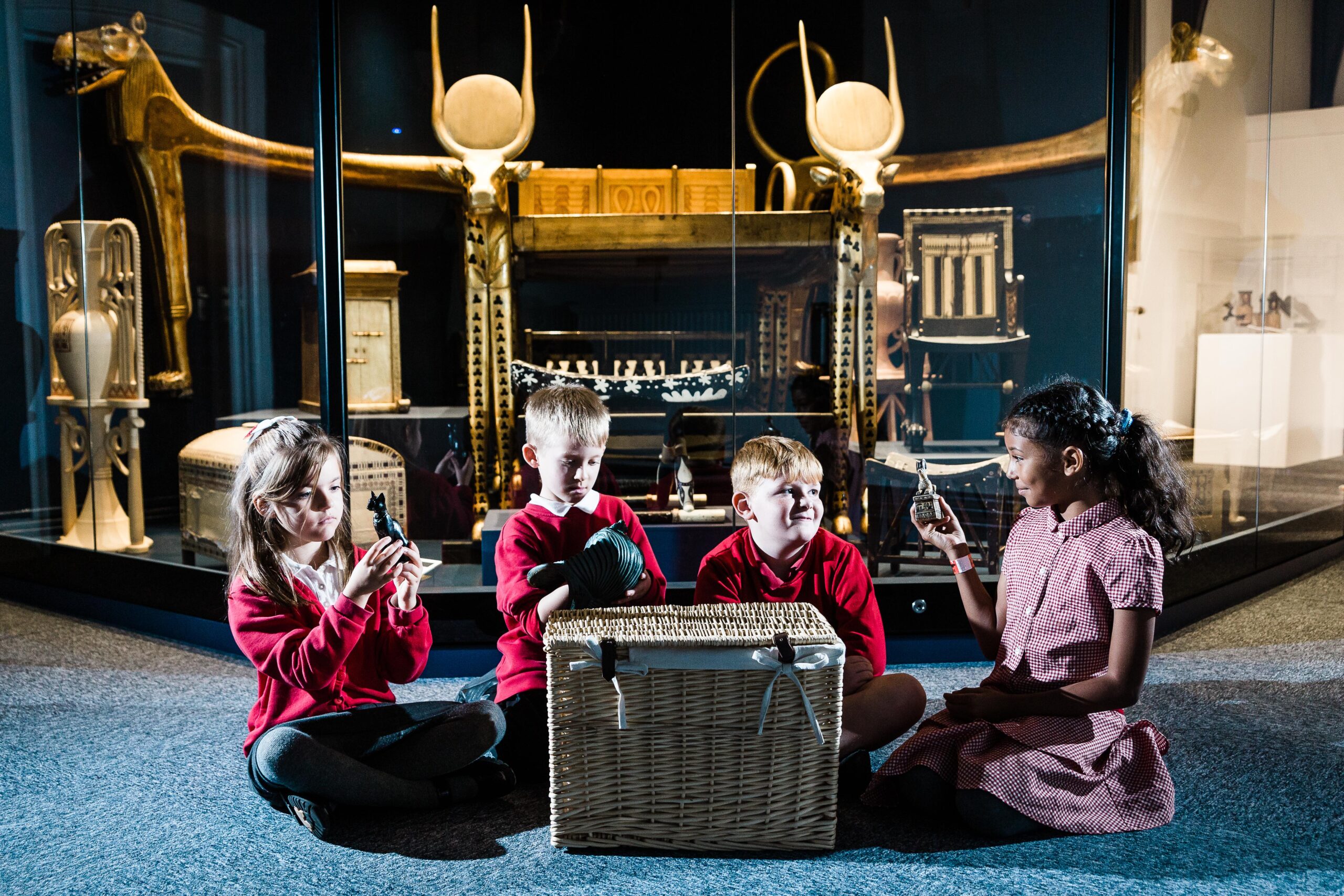 4 school children look at objects in front of a basket in a museum setting