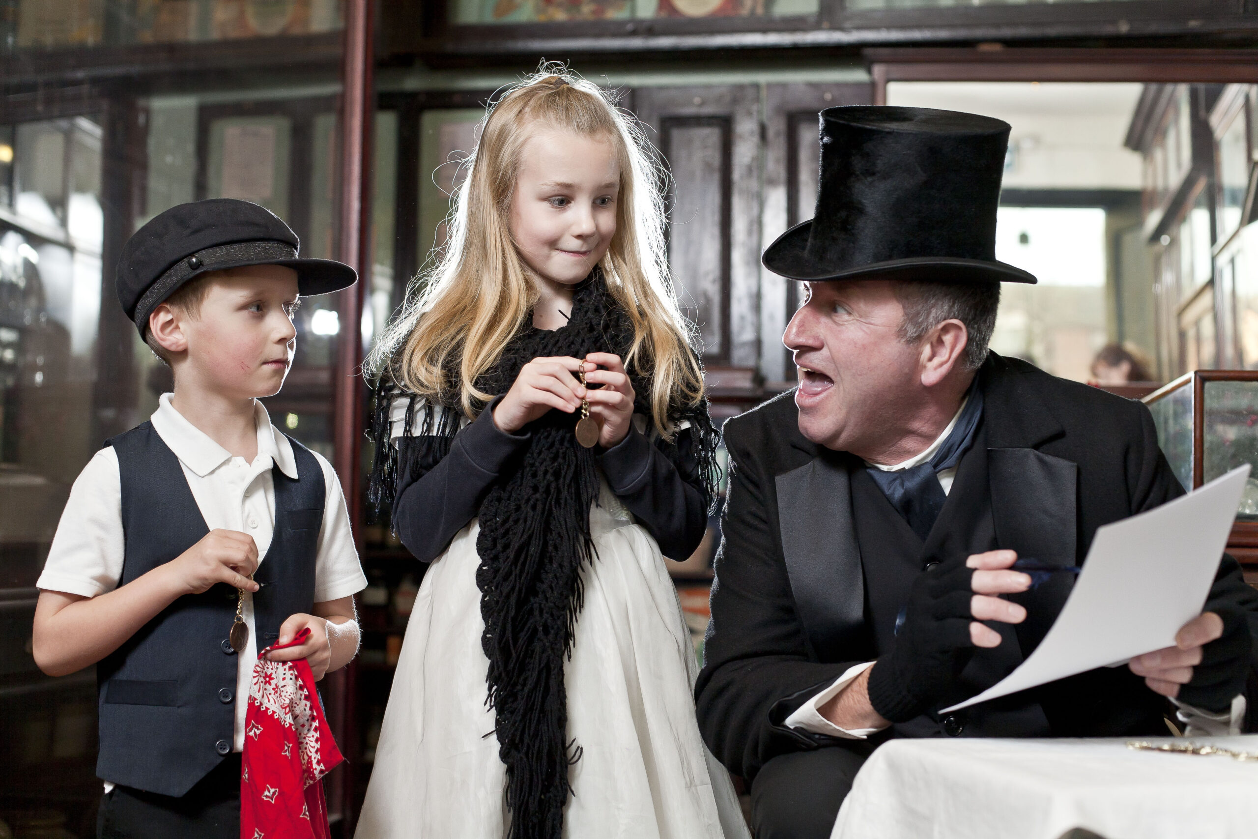 A man talks to 2 children, all in Victoria dress