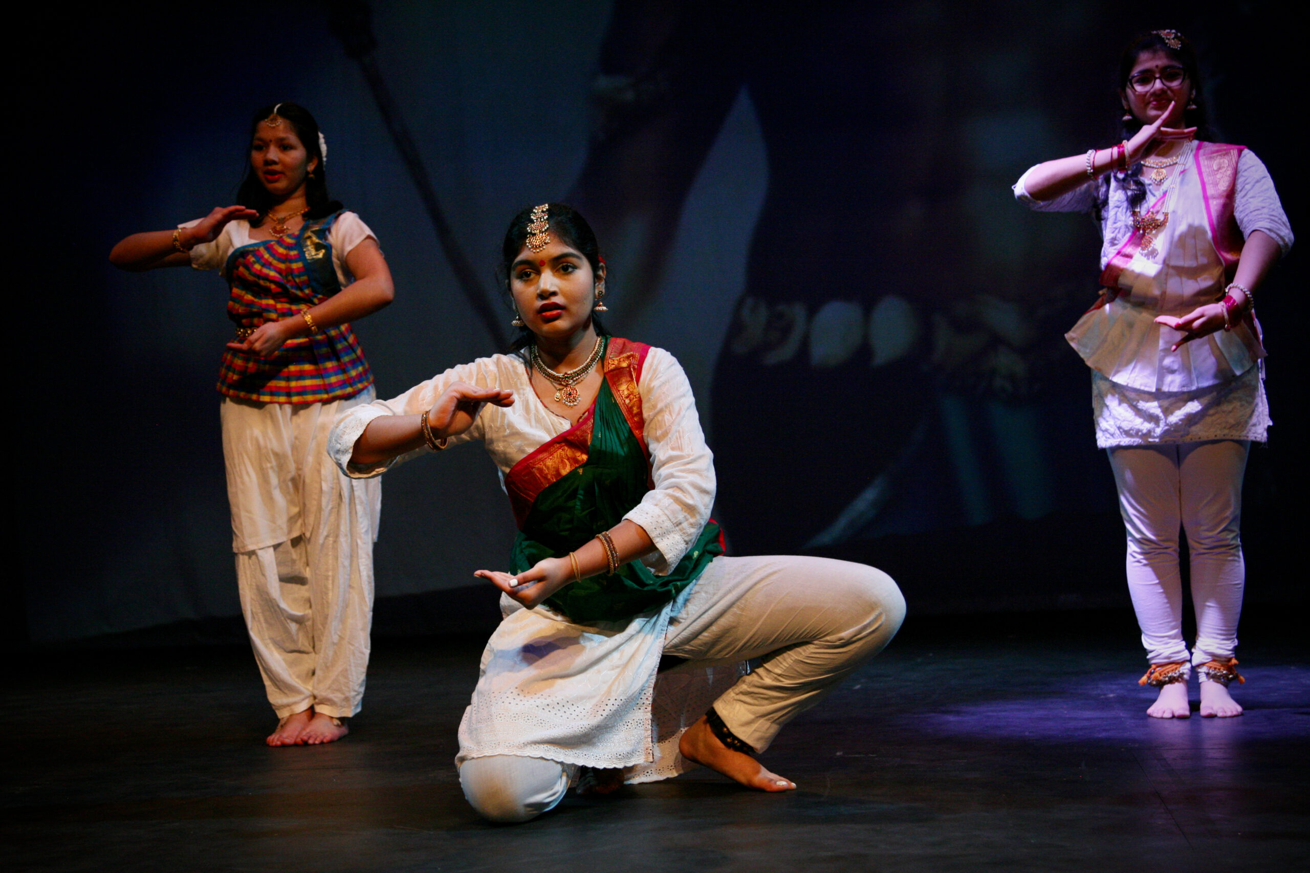 three female dancers in Indian dance costumes pose on stage