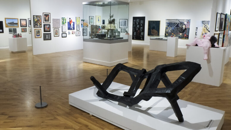 A landscape image of an gallery with frames on the wall and a black abstract sculpture in the foreground.