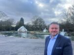 an image of Cllr Dave McCobb at Pearson Park. He is in the foreground and is smiling. Behind him you can see the park's duck pond, fountains and conservatory.