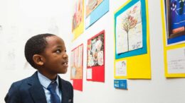 Little boy in a shirt and tie looking at pictures on a white wall