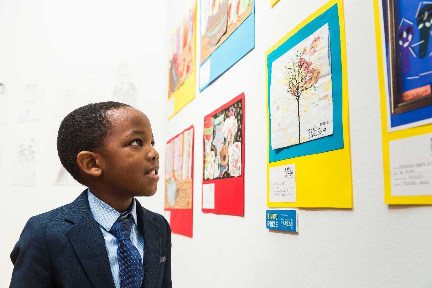 Little boy in a shirt and tie looking at pictures on a white wall