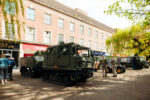 A military vehicle parked in a pedestrianised street with personnel stood with it.