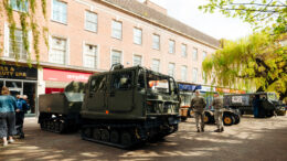 A military vehicle parked in a pedestrianised street with personnel stood with it.