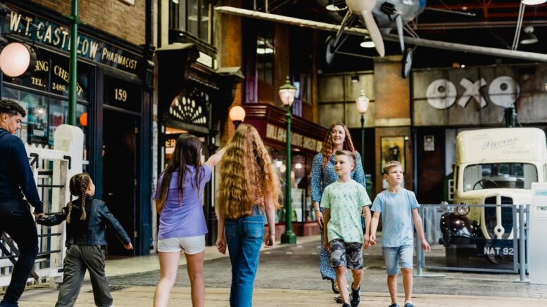 Children and adults walking through the streetlife museum with a vintage car in the background and plane suspended from the ceiling