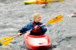 a young girl in a kayak smiles as she uses the paddle