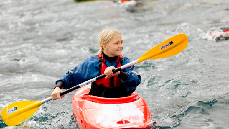 a young girl in a kayak smiles as she uses the paddle