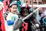 A child poses with a person in a suit of armour holding a sword and shield