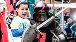 A child poses with a person in a suit of armour holding a sword and shield
