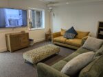 The living room has a yellow sofa and a green sofa, with a TV and patterned foot stool.