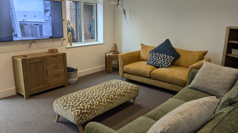 The living room has a yellow sofa and a green sofa, with a TV and patterned foot stool.