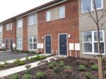 An image of newly-built terraced houses in Hull. They have blue doors and front gardens which are newly-planted.