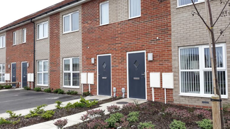 An image of newly-built terraced houses in Hull. They have blue doors and front gardens which are newly-planted.