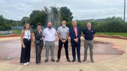 4 men and 2 women representatives from HCC, HCAL and Splash Pad Enterprises stand in front of a new splash pad with water jets spraying behind them