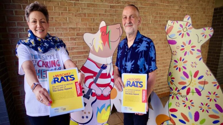 two people stand with two large cut outs if cartoon rats