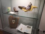 A glass museum case with football boots, a plaque and football programme on display