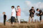 A group of 3 men and 2 young boys with camera equipment. In long grass